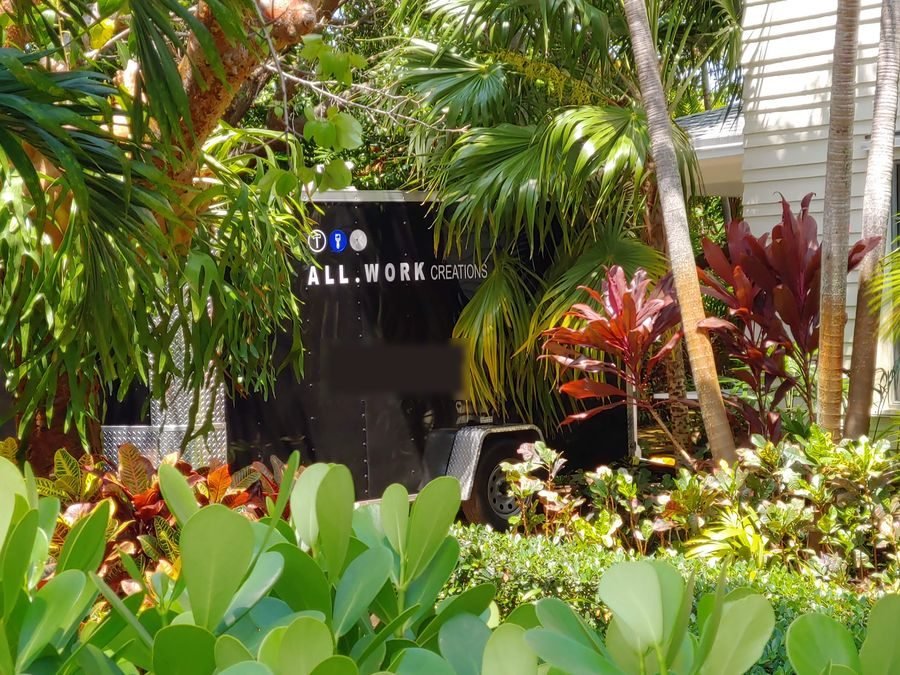 The All Work Creations trailer parked on a job site among tropical plants